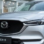 Srebrna Mazda CX-5 – zbliżenie na przód auta z widocznym grillem i reflektorami, w tle rozmyte tło salonu.