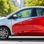 Nowoczesna Toyota Yaris w kolorze srebrnym zaparkowana na słonecznej ulicy w tle z rozmytą miejską architekturą.