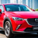 Czerwona Mazda CX-3 widziana z przodu na tle rozmytej ulicy w słoneczny dzień.