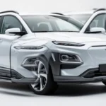 Nowoczesny srebrny SUV Hyundai Kona sfotografowany pod kątem z przodu na minimalistycznym jasnym tle.