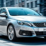 Nowoczesny hatchback Peugeot 308 III w kolorze srebrnym, widoczny od przodu, na tle rozmytej ulicy miejskiej.