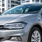 Srebrzystoszary Volkswagen Polo VI zaparkowany na ulicy, widok na przód z reflektorami LED i nowoczesną architekturą w tle.