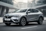 Srebrne Renault Arkana zaparkowane na asfaltowej drodze na tle nowoczesnej architektury miejskiej.
