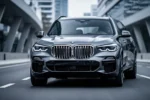 Metalicznie szare BMW X5 G05 zaparkowane na nowoczesnej drodze asfaltowej na tle rozmytej miejskiej architektury.
