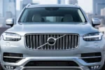 Przód srebrnego Volvo XC90 II z widocznym eleganckim grillem i światłami LED na tle miejskiego krajobrazu.