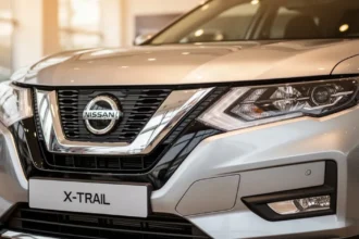 Zbliżenie na srebrny przód Nissana X-Trail IV z widocznymi reflektorami i wlotem powietrza w salonie samochodowym.