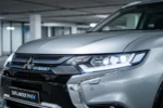 Srebrny Mitsubishi Outlander PHEV z nowoczesnymi reflektorami LED w minimalistycznym salonie.